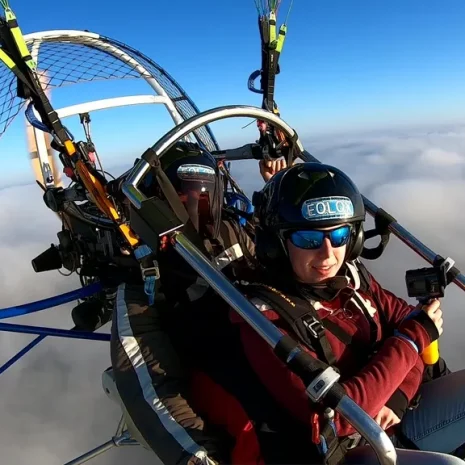 Pasajera feliz en un vuelo en paramotor sobre un mar de nubes simbolizando el mejor paramotor precio para una experiencia biplaza.