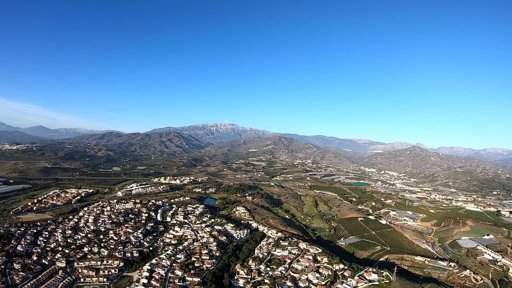 Paisaje aéreo de montañas, valles y pueblos blancos, visto desde un vuelo en paramotor en un día despejado.