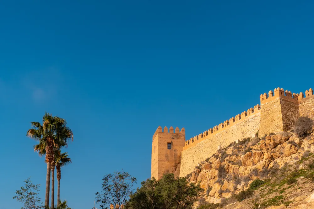 Murallas de la Alcazaba y palmeras bajo un cielo azul, una de las actividades en Málaga con más historia para visitar.