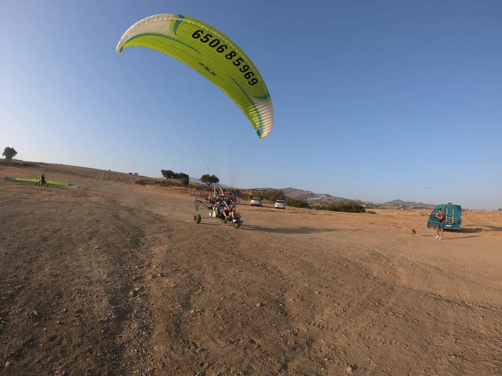 Paramotor con ruedas y dos personas preparadas para el despegue de un vuelo en paramotor desde un campo de tierra.