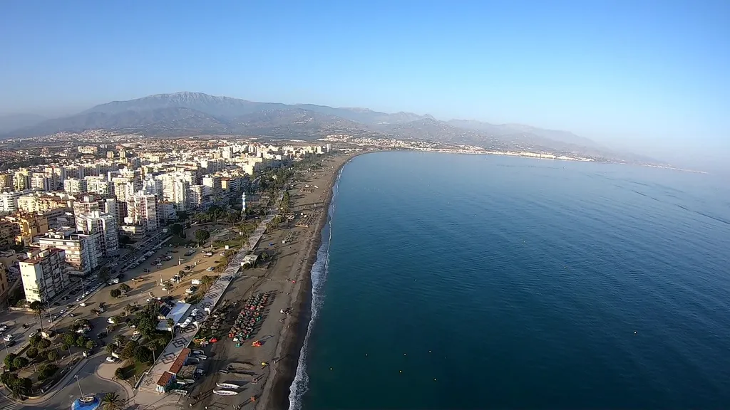 Vuelo en paramotor a lo largo de una playa de Torre del Mar, Benajarafe, Fuengirola, mostrando la línea de edificios, el paseo marítimo y el mar.