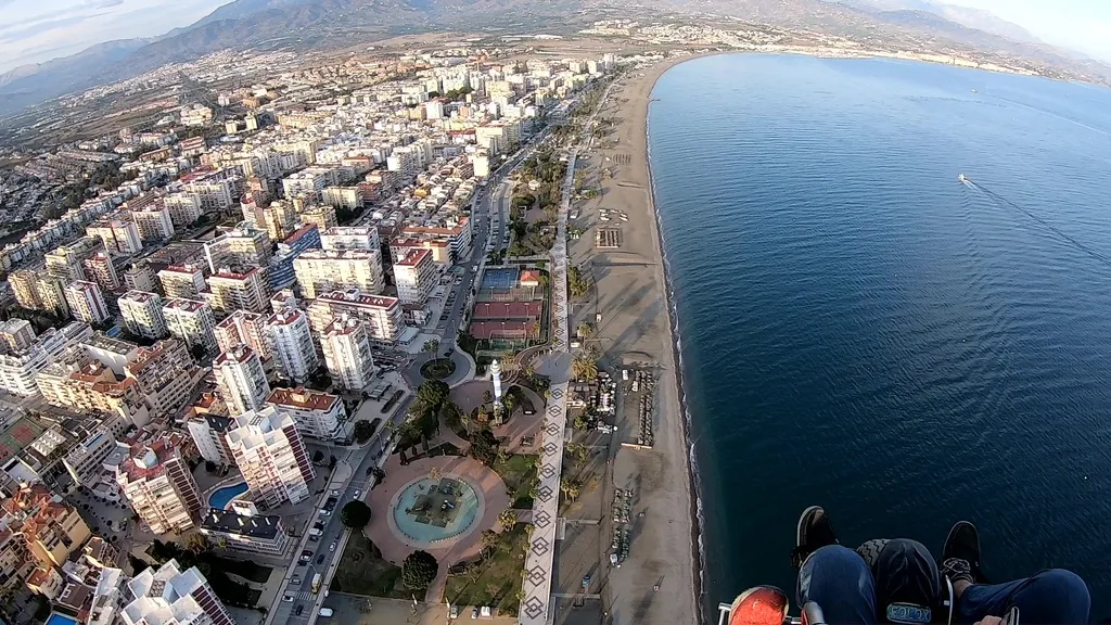Punto de vista desde un vuelo en paramotor sobrevolando una ciudad, con la playa debajo de los pies del piloto